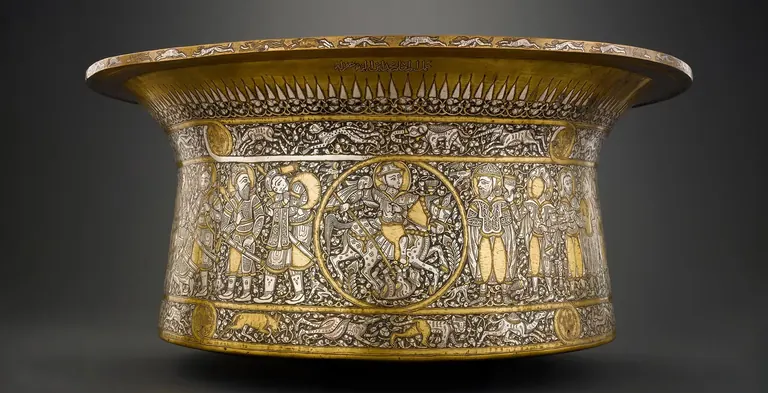 A gold basin inlaid with delicate and detailed silver designs of humans and animals surrounded by vines.
