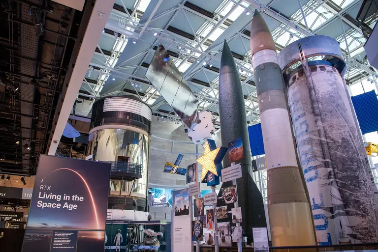 A gallery with several large rockets on display, an RTX Living in the Space Age sign in front and the Skylab Orbital Workshop visible behind