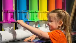 A young girl interacting with rainbow-coloured tubes in the Making Waves exhibit