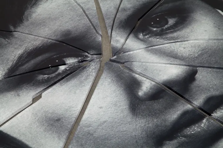 A detail shot of a black-and-white image of a person's face printed on plexiglas that has been shattered in the center.