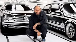 L’artiste Joshua Vides accroupi entre deux voitures peintes à la main dans son style de contours noirs et blancs