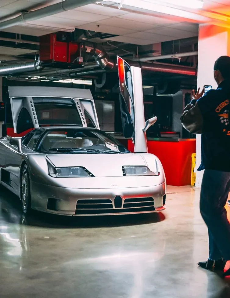 Bugatti EB110 argentée aux portes en élytre levées dans The Vault ; un visiteur la photographie