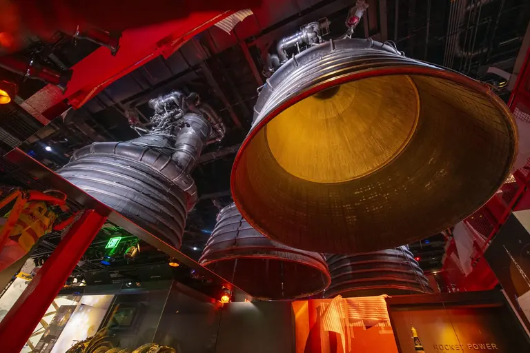 A large metal dome-like spacecraft structure seen from below, hanging from the gallery ceiling, with mirrors multiplying the reflection