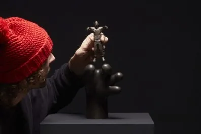 Frankey col·loca una petita figura de bronze sobre una escultura negra surrealista, part de Planet Positive Disruption, al Moco Museum Amsterdam