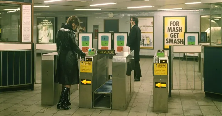 Una imatge històrica d’un vestíbul de bitllets del metro de Londres, amb dues persones travessant els torniquets