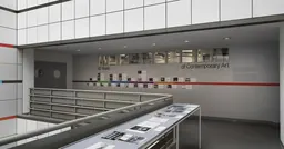 A large vitrine encasing black and white photographs in the middle of an open atrium, with a colourful illustrated timeline adhered to the wall behind