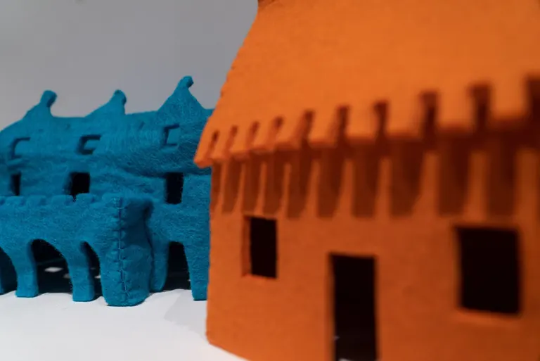 Detail of Laure Tixier's Plaid Houses maquettes: an in-focus blue felt house with visible stitches and coarse texture beside an out-of-focus orange one.