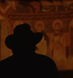 Silhouette of a visitor in front of a Romanesque church mural, image for The Reverse Journey by Ona Balló