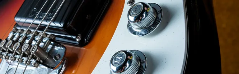 Primer pla del pont, la pastilla i els comandaments cromats d’una guitarra elèctrica amb motiu de raigs de sol