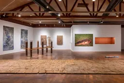 Vue de l’installation « tierra » au Craft Contemporary : un sol en briques de terre, une sculpture en bois et en corde et des œuvres murales