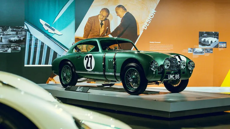 Voiture de course Aston Martin ancienne, verte, numéro 27, sur un socle devant des visuels consacrés au design Aston Martin