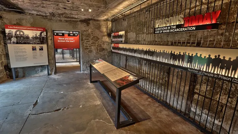 Eingang zur Ausstellung Prisons Today im Eastern State Penitentiary; Steinmauer mit senkrechten Metallstäben; Silhouetten zeigen die Zahl der Gefangenen pro 100.000 Amerikaner.