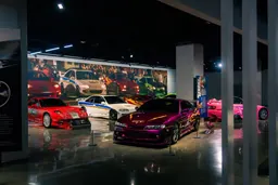 Salle présentant des voitures des films Fast & Furious, dont une Nissan S14 violette, une RX-7 rouge et une S2000 rose, devant une fresque composée d’images de films