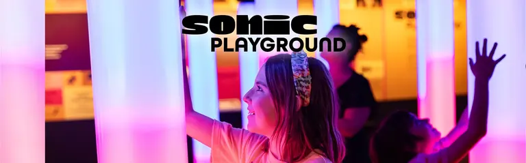 Una nena amb una diadema toca una columna de llum rosa i blava que brilla a la galeria Sonic Playground