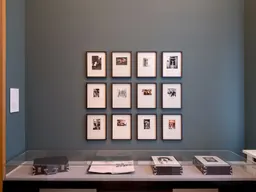 Installation view of Helmut Newton's One-off Album: a grid of hand-annotated prints above a vitrine holding the album