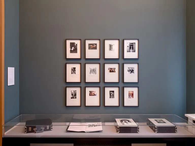 Installation view of Helmut Newton's One-off Album: a grid of hand-annotated prints above a vitrine holding the album