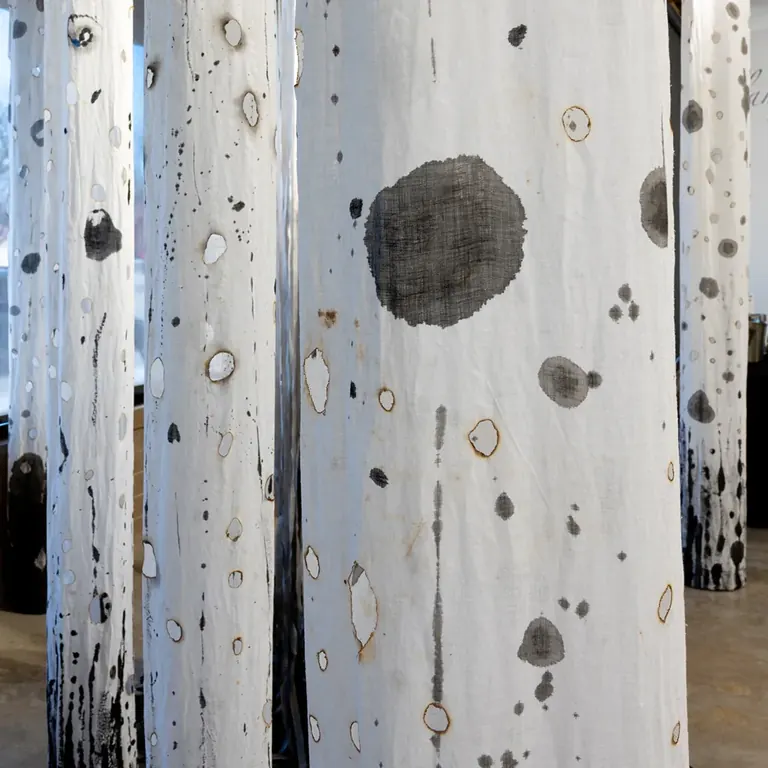 Katherine Steichen Rosing, Harbingers - tattered white linen columns charred with flame, suspended as a ghost forest