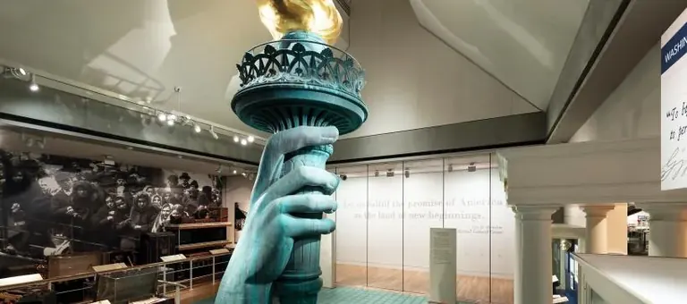 Nachbildung der Fackel tragenden Hand der Freiheitsstatue zwischen Einwandererfotografien von Ellis Island