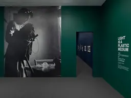 Entrance to Light Is a Plastic Medium at the Hirshhorn: a wall-size photograph of Carlotta Corpron at work beside green title walls