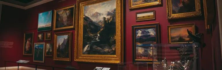 Mur de galerie couvert, selon un accrochage de type salon, de peintures de paysages de l’Ouest aux cadres dorés ; au centre, une grande scène de cascade en montagne
