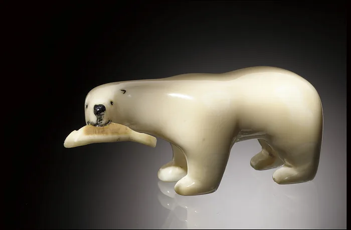 Carved stone polar bear figurine holding a fish, displayed in Window on Collections