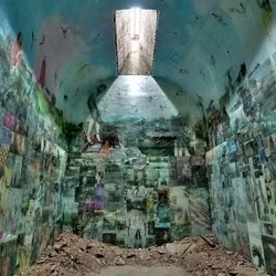 Installation von Jesse Krimes: „Apokaluptein16389067:II“ in einer Gefängniszelle; Foto-Collagen bedecken Wände und Decke, ein Oberlicht fällt auf Trümmer am Boden.