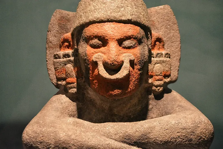Sculpture mexica en pierre représentant un personnage au visage peint en rouge et aux bras croisés, salle 6 du Museo del Templo Mayor