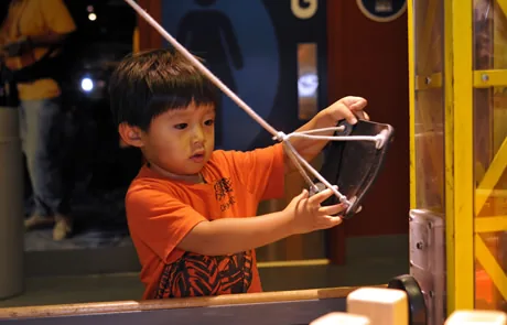 A young child pulling a rope on a yellow-framed rig in the Construction Zone exhibit at Boston Children's Museum