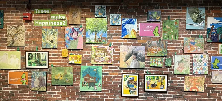 Trees Make Happiness 2 installation: dozens of small paintings and drawings by Japanese student artists hung on a brick wall in the Japanese House Gallery