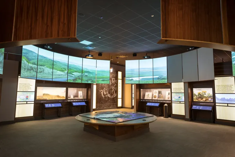 La primera galeria del Cyrus Tang Hall of China, amb una taula amb un mapa en primer pla i un gran cercle de pantalles de vídeo damunt les vitrines de l’exposició.