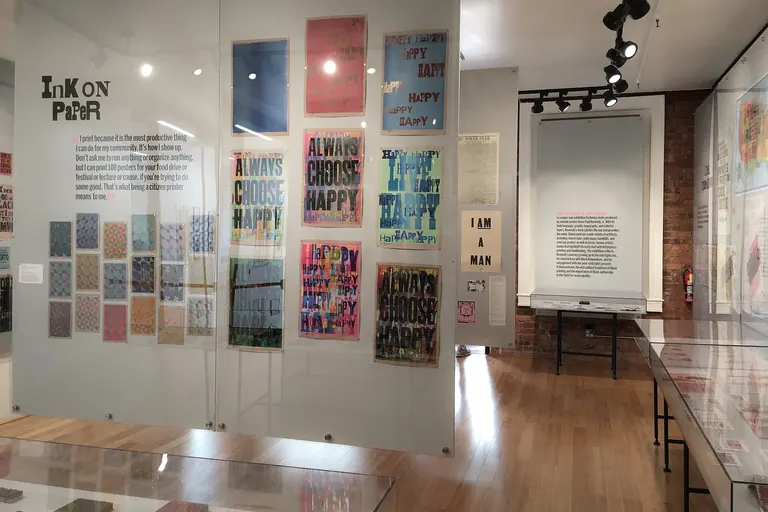 Galerie de Letterform Archive, avec des affiches imprimées en typographie par Amos Paul Kennedy, Jr. sur des panneaux de verre et des vitrines devant un mur de briques