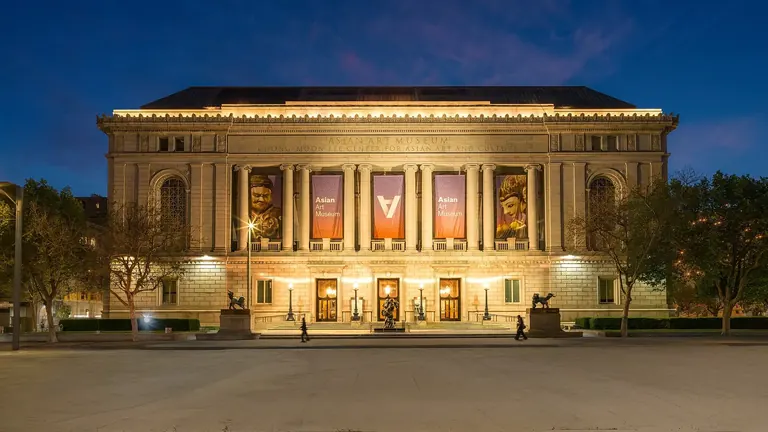 Façade Beaux-Arts de l’Asian Art Museum, sur Larkin Street, illuminée au crépuscule, avec des bannières entre ses colonnes