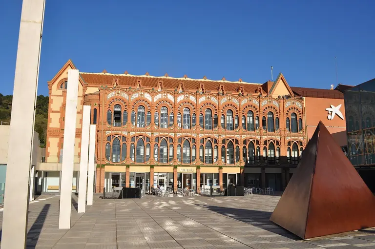 The red-brick Modernista facade of CosmoCaixa with a rust-coloured pyramid sculpture in the plaza