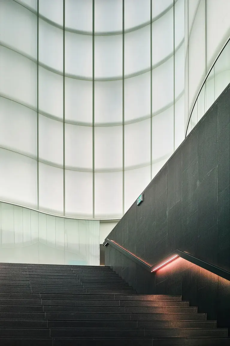 Escalier montant vers l’Agorà de verre illuminée du MUDEC, conçue par David Chipperfield