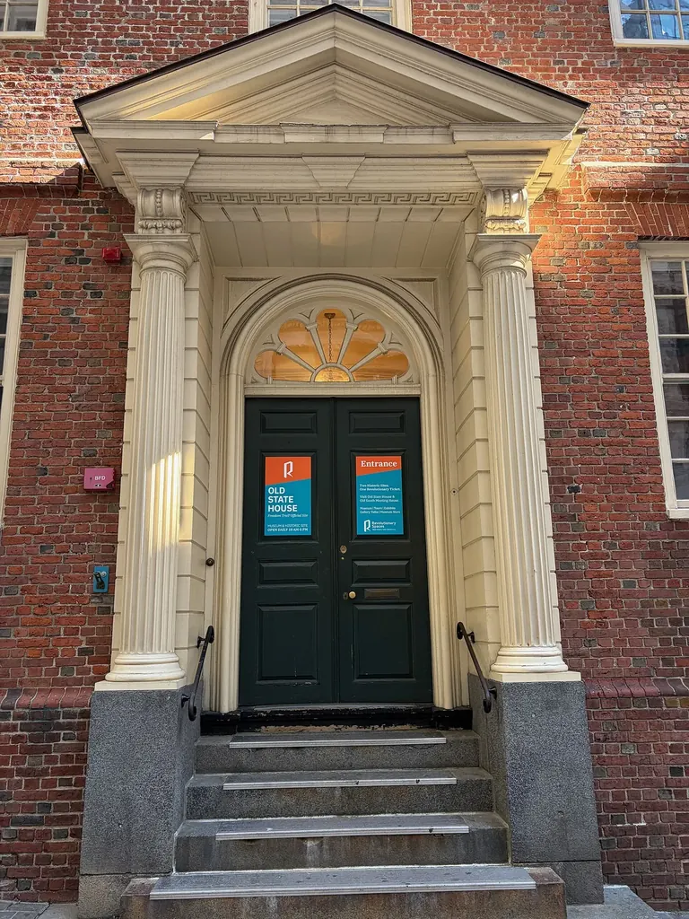 The brick facade and entrance of the 1713 Old State House on Washington Street in downtown Boston, framed by modern office towers