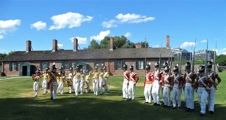 Un corps de fifres et tambours et des reconstituteurs en tunique rouge défilent devant une caserne en briques de 1815 à Fort York, à Toronto