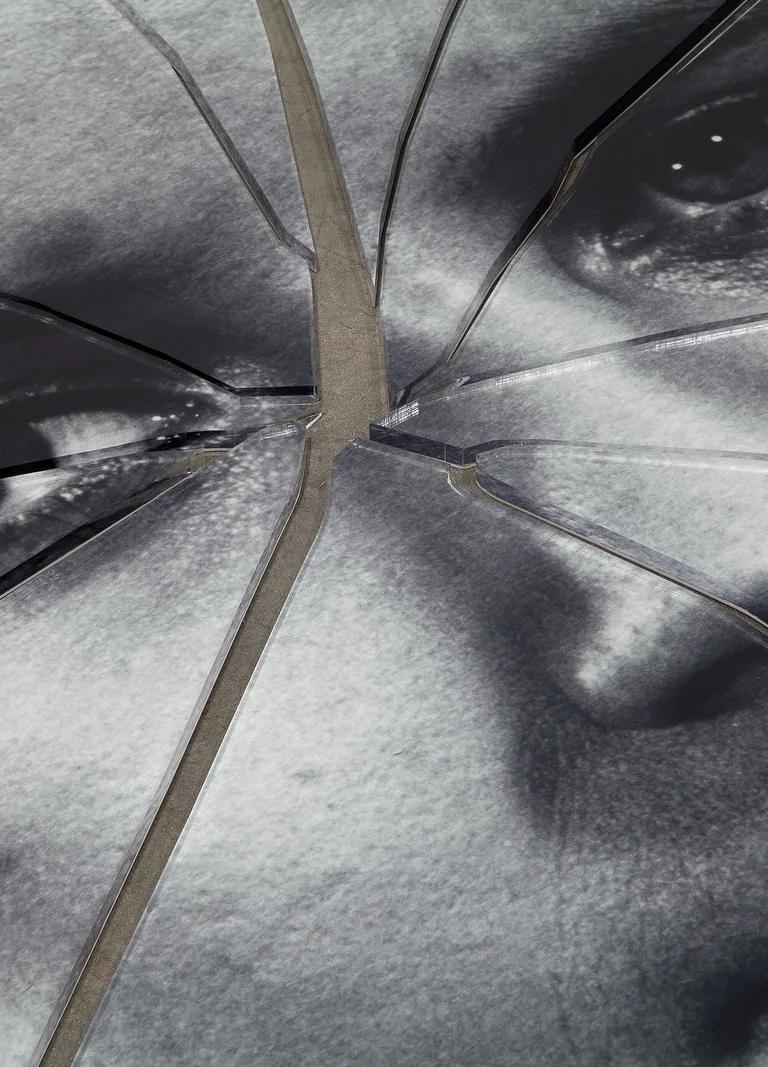 A detail shot of a black-and-white image of a person's face printed on plexiglas that has been shattered in the center.