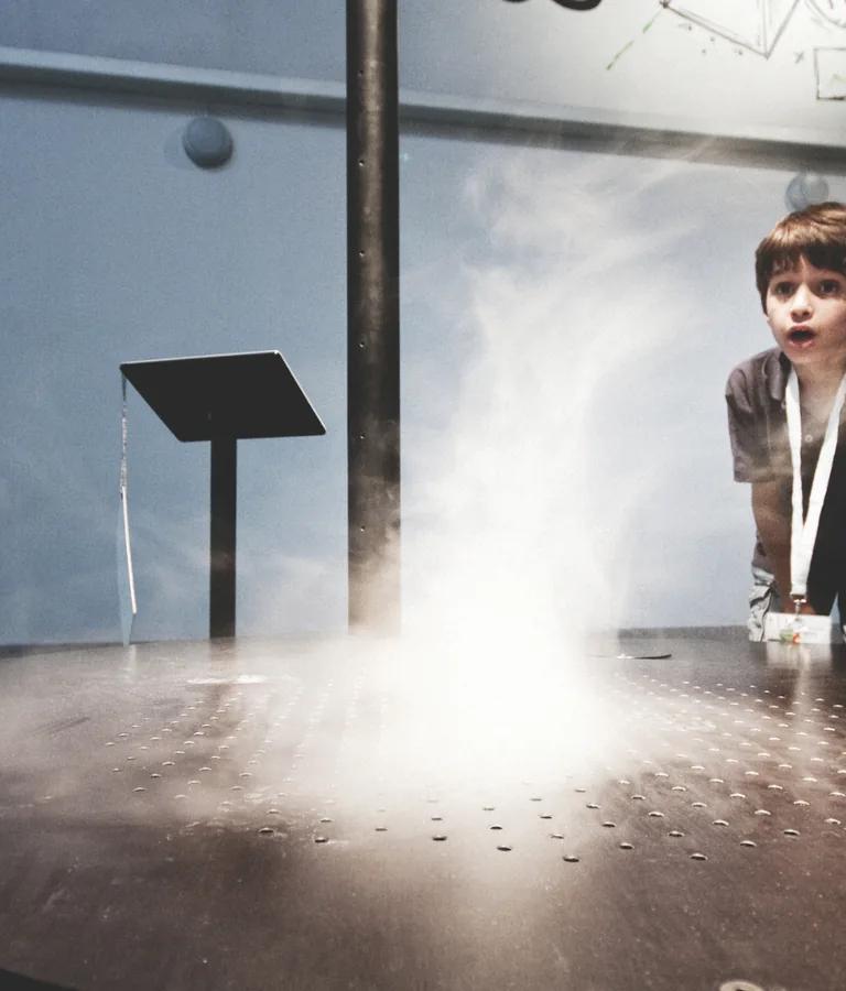 A child watching a vortex of mist rise from the tornado exhibit in Explora