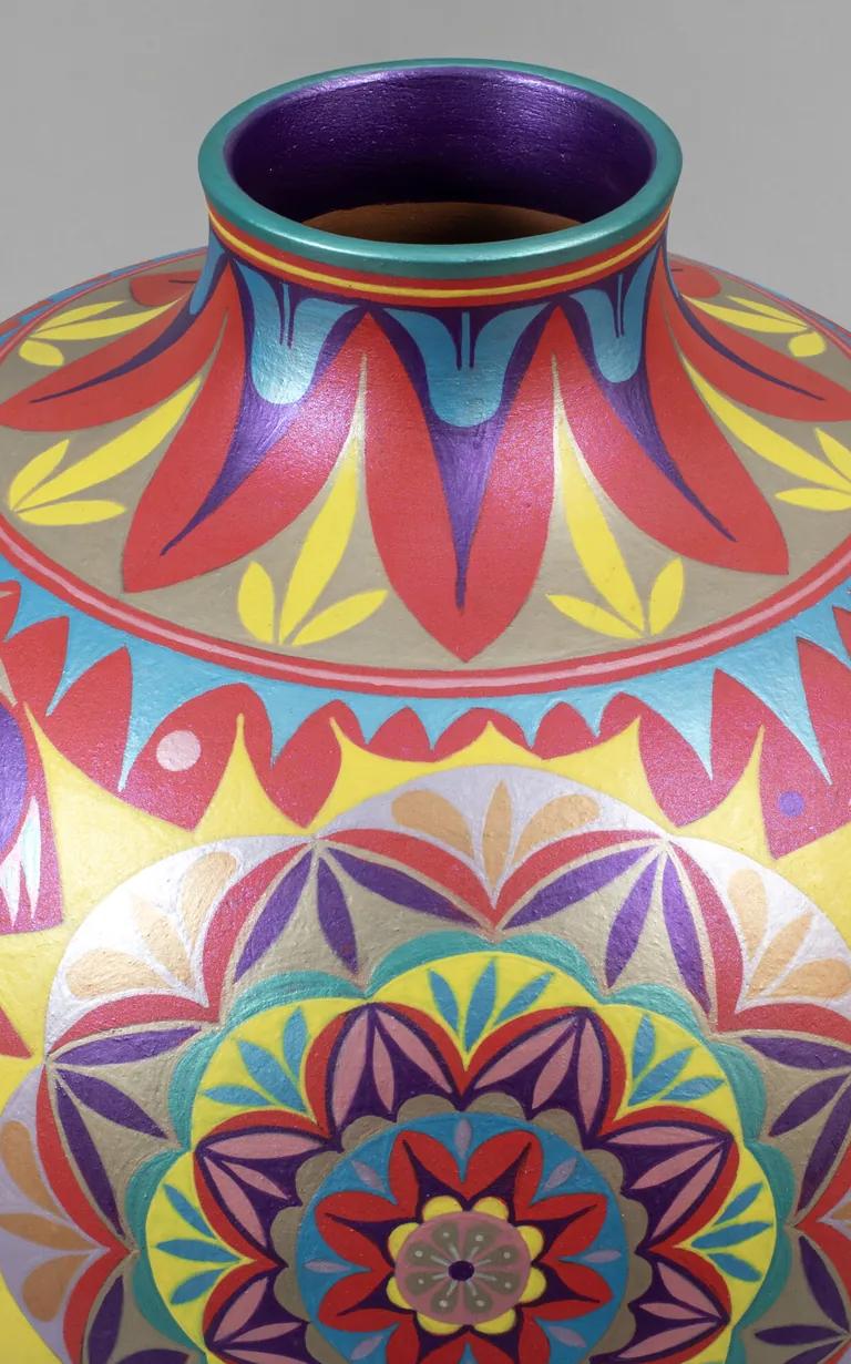 A round ceramic vase with a short neck decorated with intricate geometric and floral patterns painted in red, pink, blue, yellow, and purple.