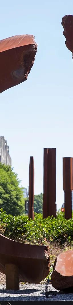 A circular, rust-colored sculpture and three rust-colored columns in the median of a city street.