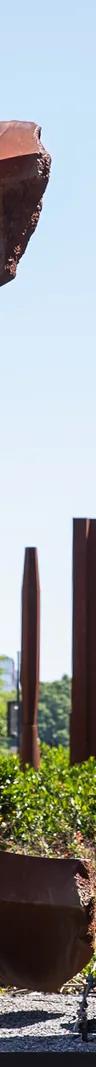 A circular, rust-colored sculpture and three rust-colored columns in the median of a city street.