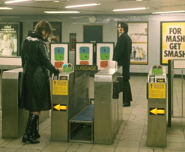 A historic image of a London underground ticket hall with two people going through the barriers