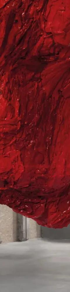 Large red textured sculpture by Anish Kapoor hanging from ceiling to floor in a columned space