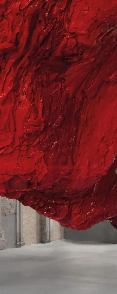 Large red textured sculpture by Anish Kapoor hanging from ceiling to floor in a columned space