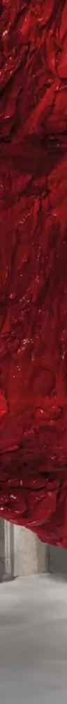 Large red textured sculpture by Anish Kapoor hanging from ceiling to floor in a columned space