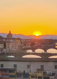 Florence skyline at dusk with Ponte Vecchio lit over the Arno River, seen from the Vasari Corridor route