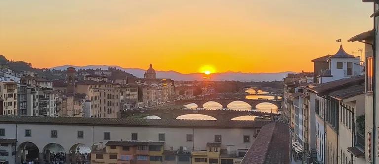Florence skyline at dusk with Ponte Vecchio lit over the Arno River, seen from the Vasari Corridor route