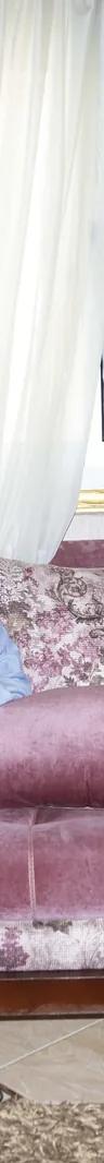 A woman on a pink floral sofa looking at her phone, from Yomna El Beyaly's series In Her Own Way