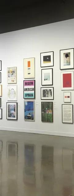 Installation view with framed artworks hung salon-style on the walls and three people looking at the art