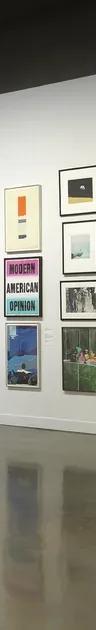 Installation view with framed artworks hung salon-style on the walls and three people looking at the art